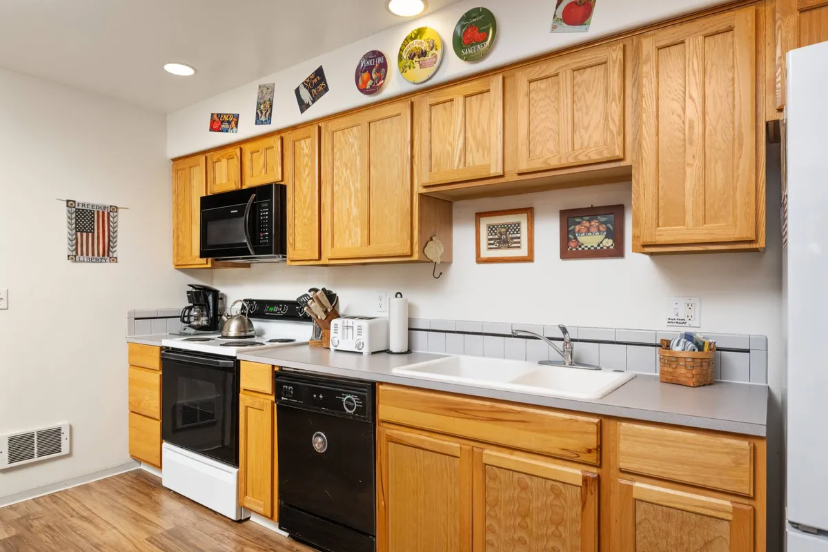 A cozy kitchen with wooden cabinets, black appliances, and a kitchen sink, accentuated by decorative plates. The layout is functional, making it ideal for both preparing meals and entertaining guests. The warm details evoke a sense of tradition and comfort.