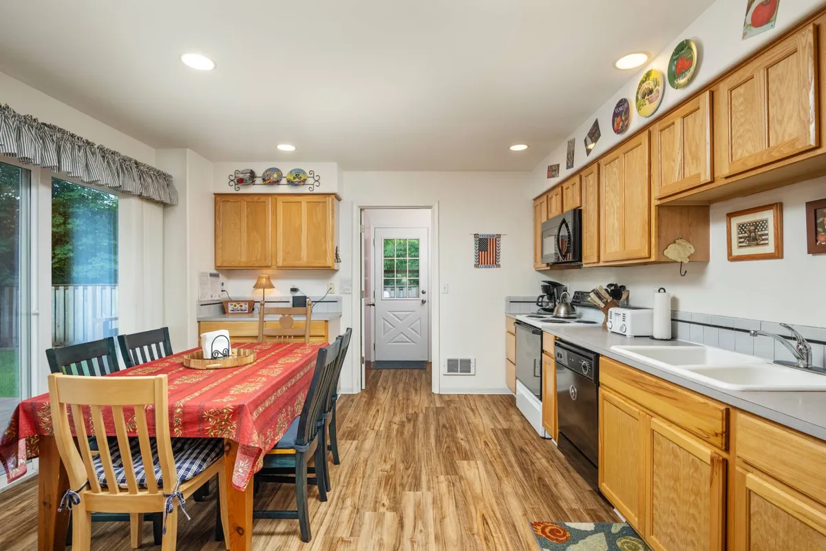 This image centers on a dining table dressed with a vibrant red tablecloth, surrounded by wooden cabinetry and visible kitchen appliances. The atmosphere is warm and homey, hinting at lively family meals and casual gatherings. The kitchen is functional and inviting, with everything close at hand for shared cooking and dining experiences.