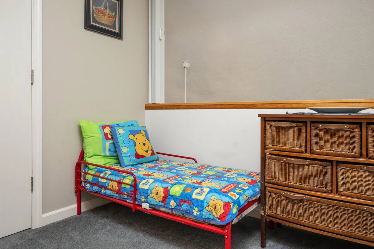 A playful and inviting bedroom featuring a bed with colorful bedding, a wicker dresser, and family-friendly decor. The space is designed for relaxation, bedtime stories, and playful moments, making it especially suitable for children or extra guests.