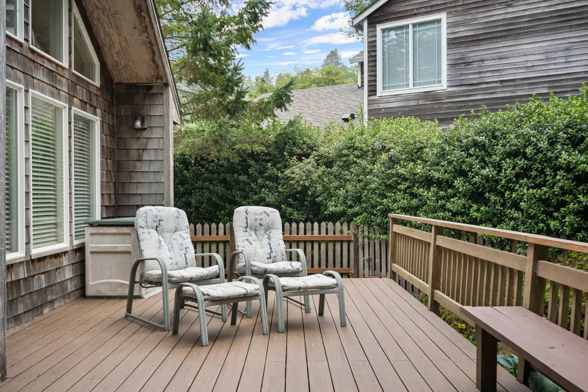 This tranquil exterior view spotlights two lounge chairs on a wooden deck surrounded by vibrant greenery, perfect for relaxing, enjoying a book, or soaking up the sun in a secure environment.