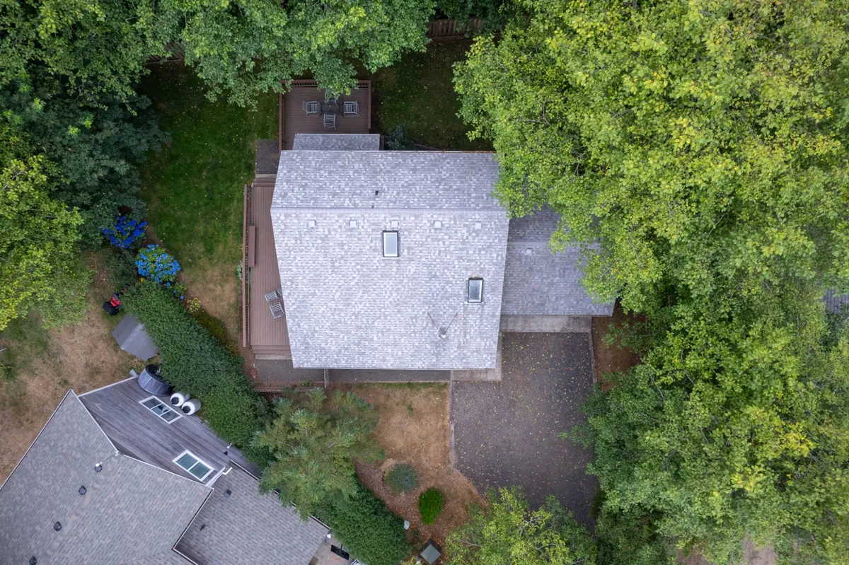 A view of the home’s exterior deck, surrounded by trees and garden space, with ample room for relaxing or hosting gatherings. The deck area is spacious and inviting, capturing the transition from outdoor adventure to home comfort, and hints at the fenced yard ideal for kids and pets.