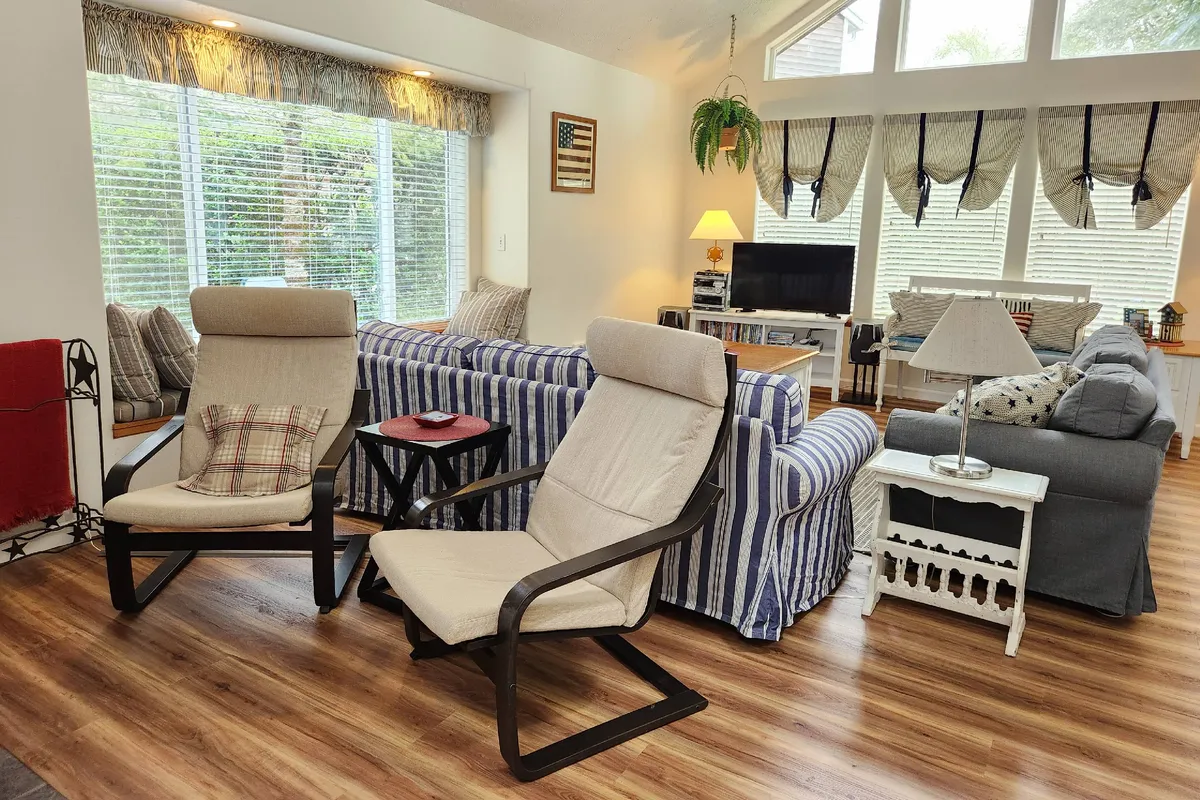 A cozy living area furnished with a striped sofa and rocking chairs, complemented by warm lamps and a television. The setting encourages relaxation and socializing after active days outside. The setup feels inviting, with subtle hints of the outdoors visible through the window and the overall bright ambiance.